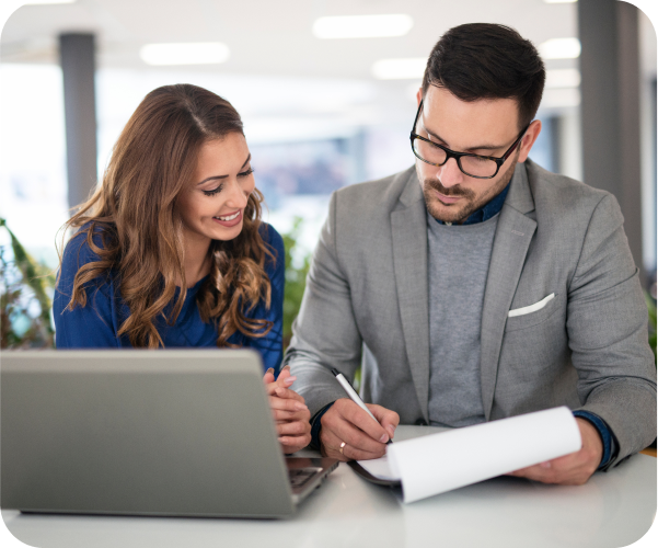 A woman and man sitting next to each other at work looking at the same paper