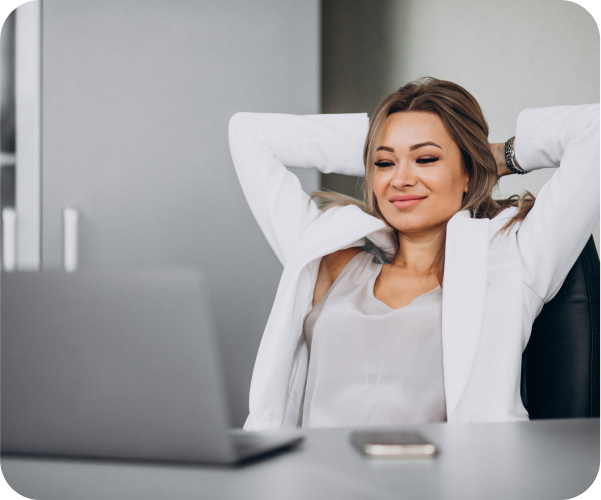 Young woman sitting at table with laptop open and her hands up behind her head
