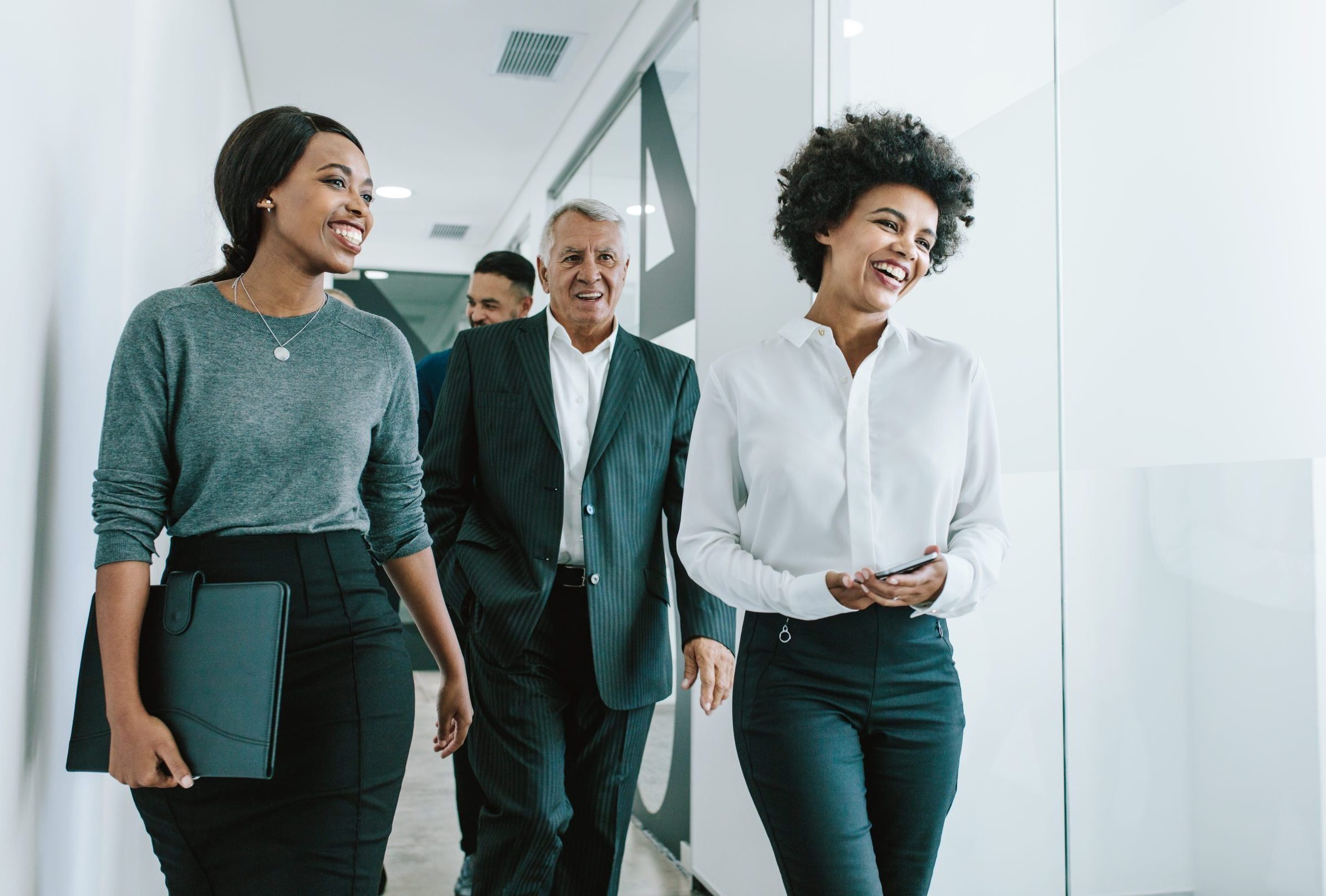 Diverse group of business people walking through office corridor. Team of corporate professionals walking and talking in modern office hallway.
