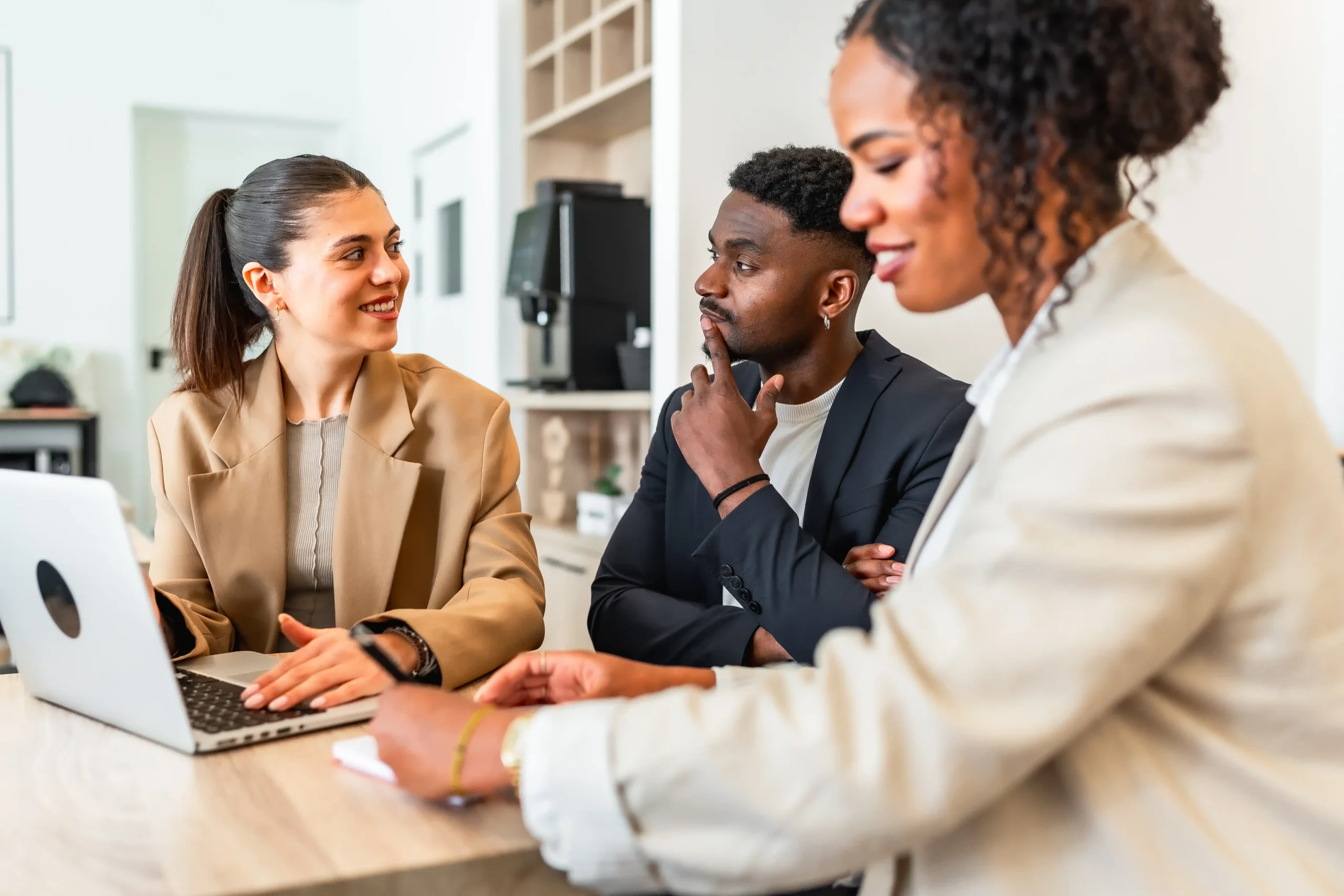 Three team members sit collaborating at a desk together in an office.