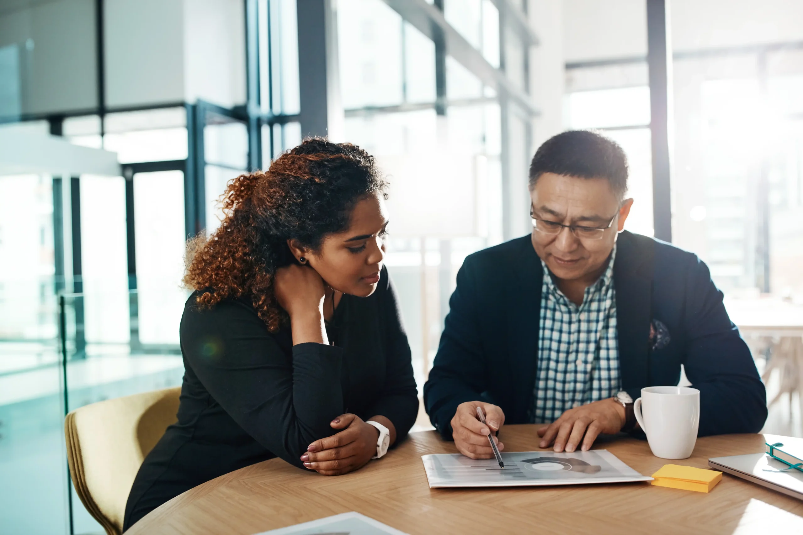 A business woman and business man sitting at a desk looking at a report together.